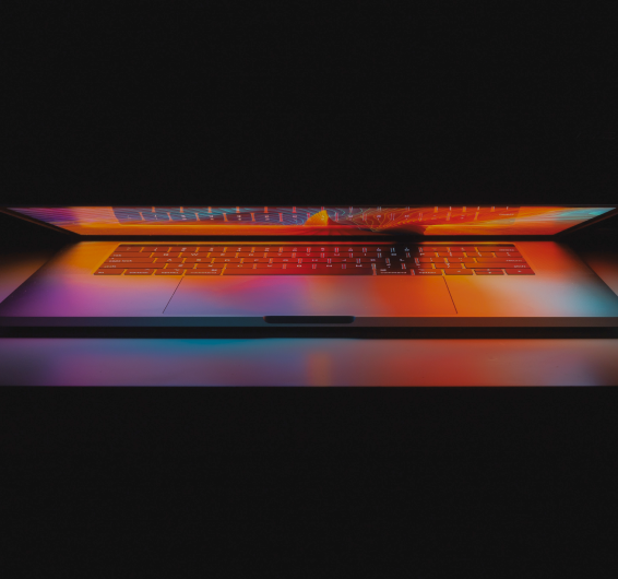 Notebook com sua tela quase fechada iluminando o teclado com cores alaranjadas