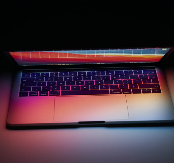 Notebook com a tela semi-aberta iluminando o teclado com cores azuis e vermelho formando um rosa no centro